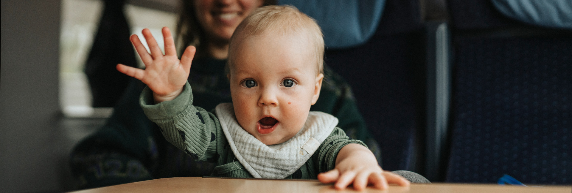 Baby waving with mother in background